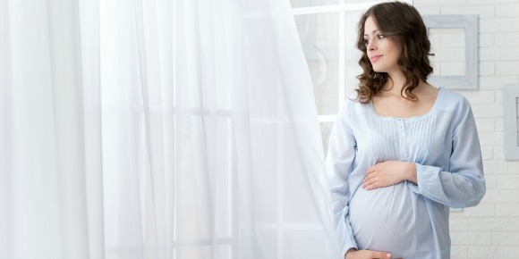カーテン脇に立つ妊娠した女性